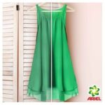 Bright green sleeveless dress on a hanger against a light pink wall, ARIEL logo in the bottom-right corner.