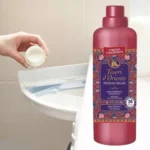 Hand pouring pink liquid detergent into a front-loading washing machine drawer beside a pink bottle labeled Tesori d'Oriente Persian Dream.